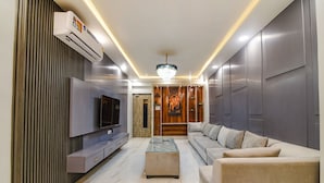 A modern living room with a flat-screen TV, a glass coffee table, a beige sofa, and a decorative wall panel. - FabHotel Icon (Danapur)