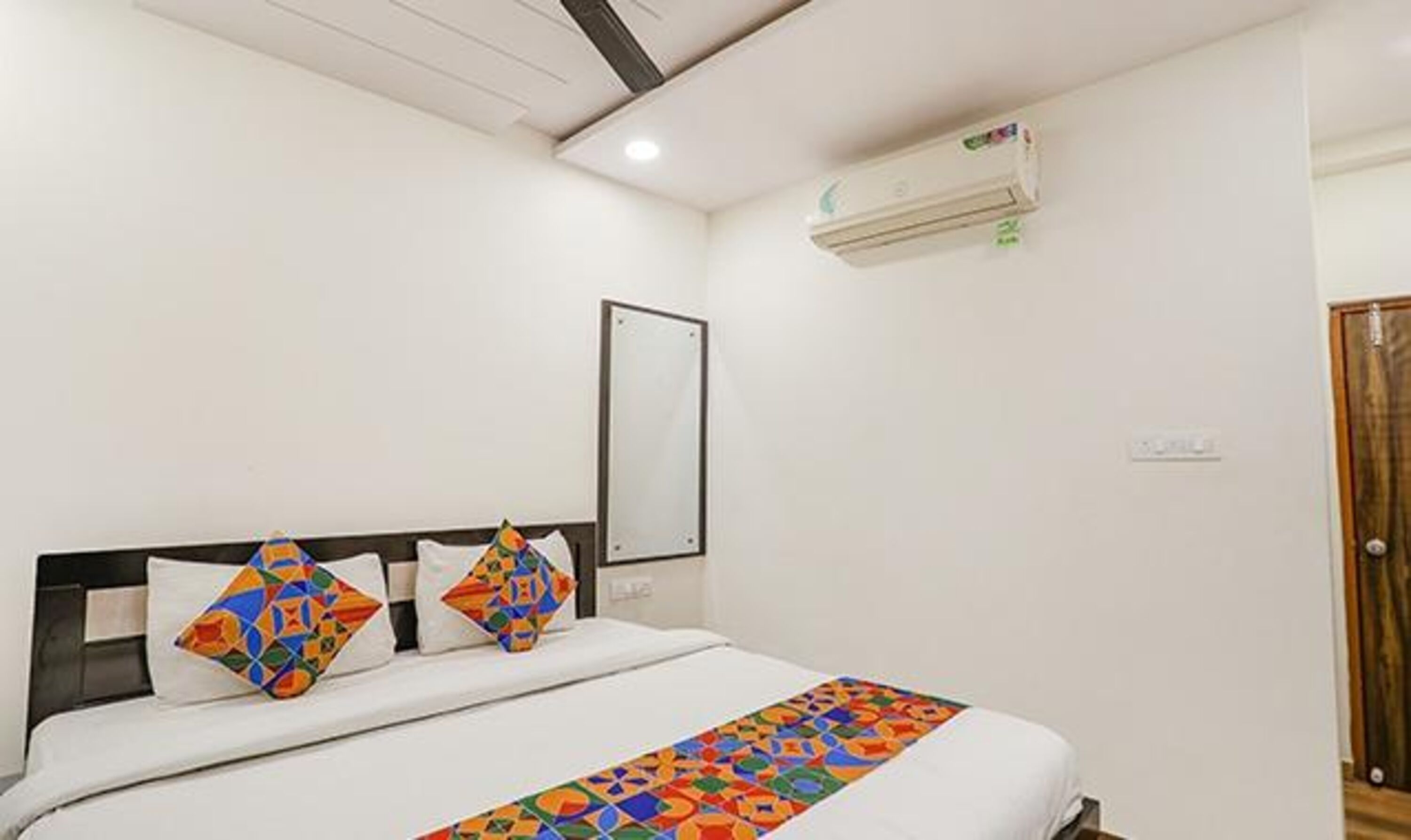 A hotel room with a bed, a wall-mounted air conditioner, and a door.