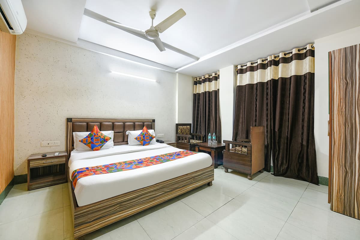 A hotel room with a large bed, a ceiling fan, a nightstand, a dresser, and a desk with a chair.