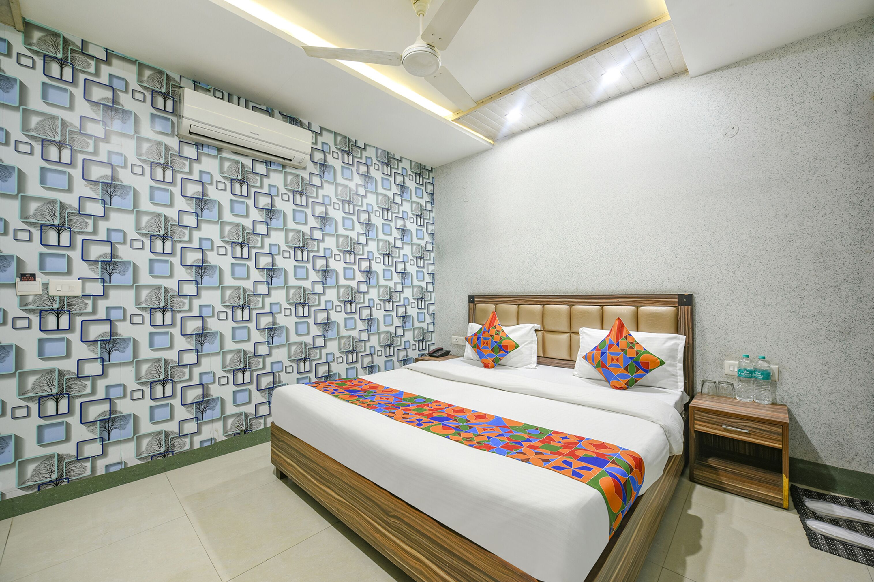 A hotel room with a bed, nightstand, and wall-mounted air conditioner.