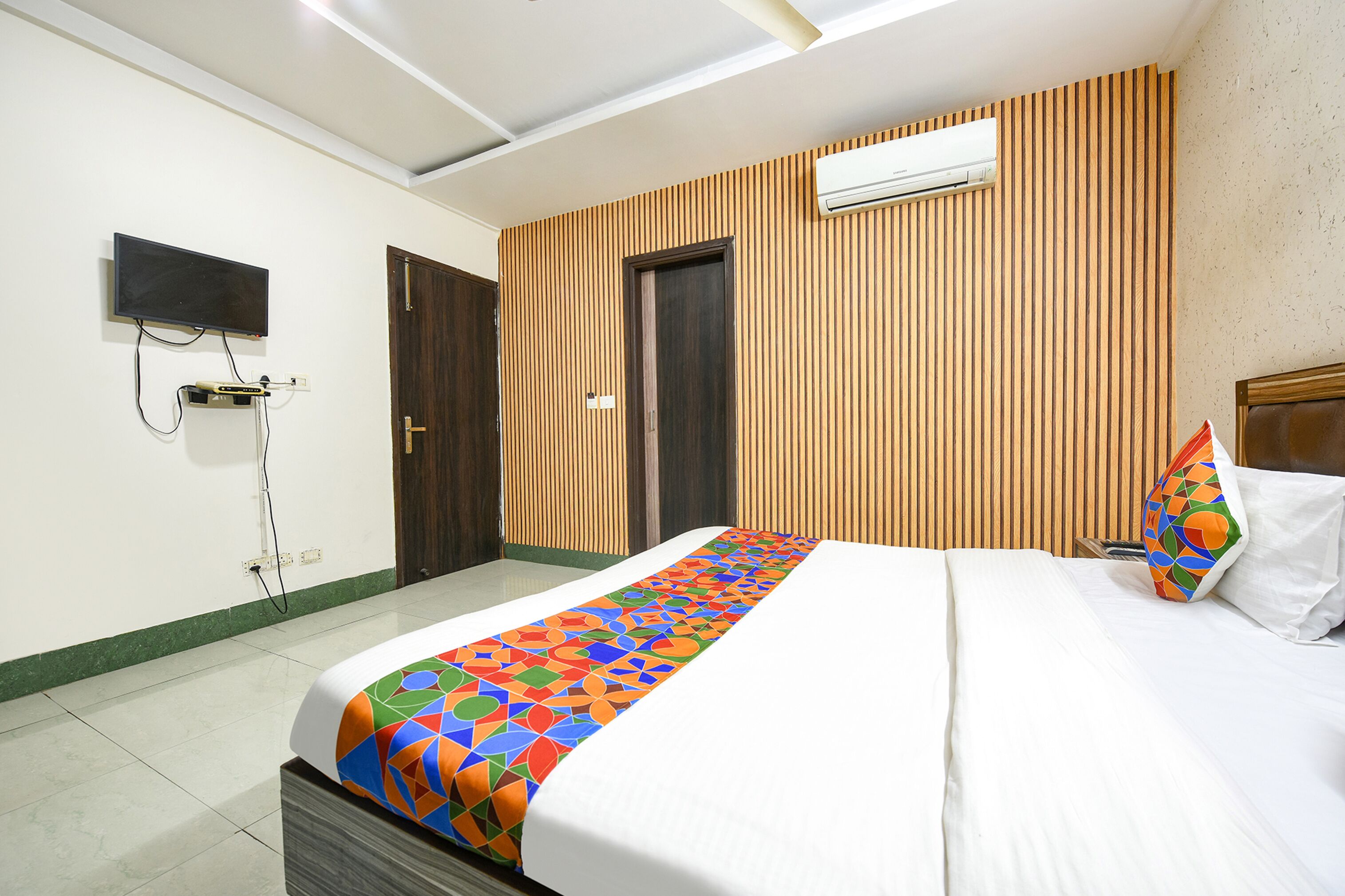 A hotel room with a bed, a TV mounted on the wall, and an air conditioning unit.