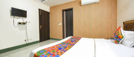 A hotel room with a bed, a TV mounted on the wall, and an air conditioning unit.