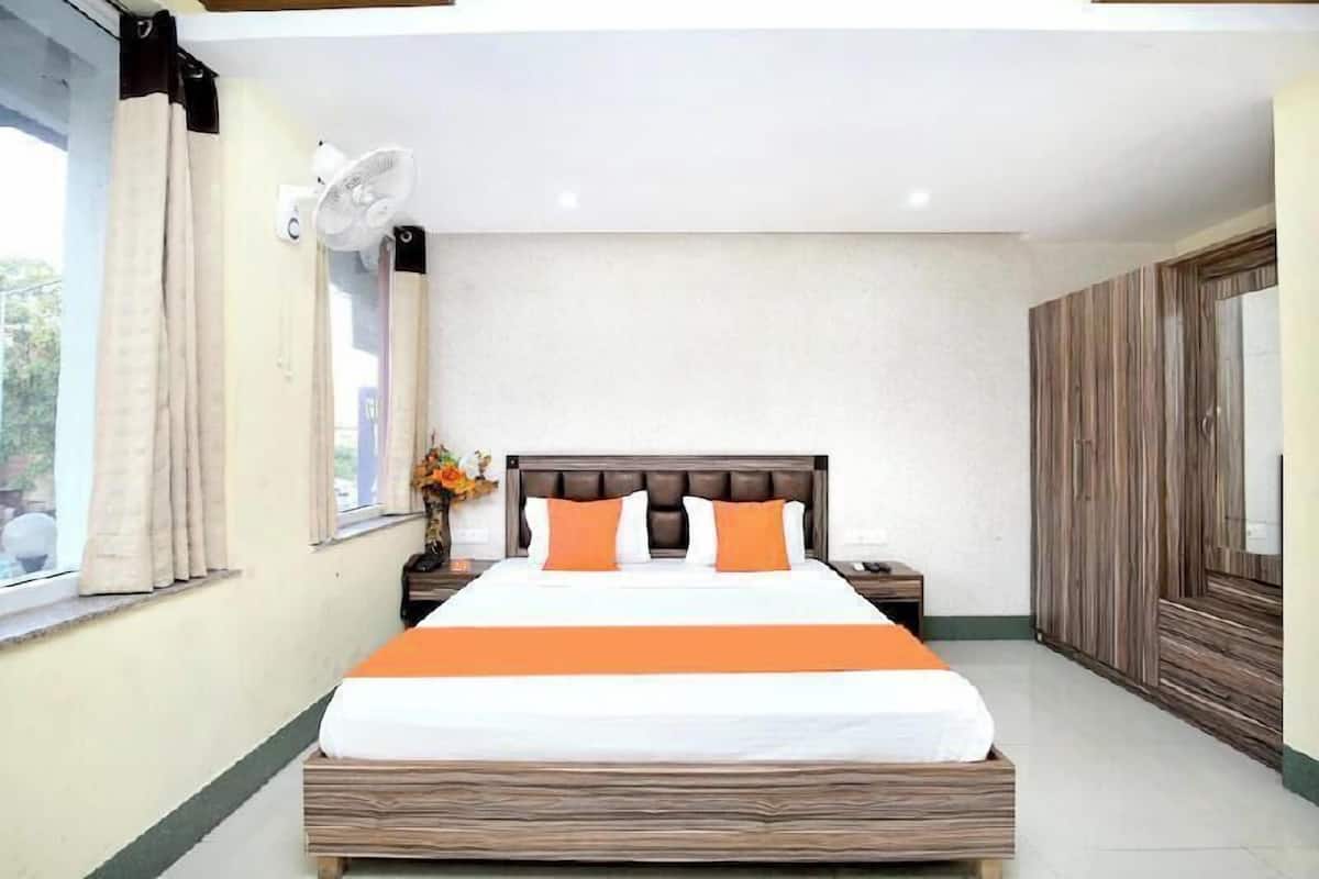 A hotel room with a large bed, a bedside table, a nightstand, a wall-mounted fan, and a window with curtains.