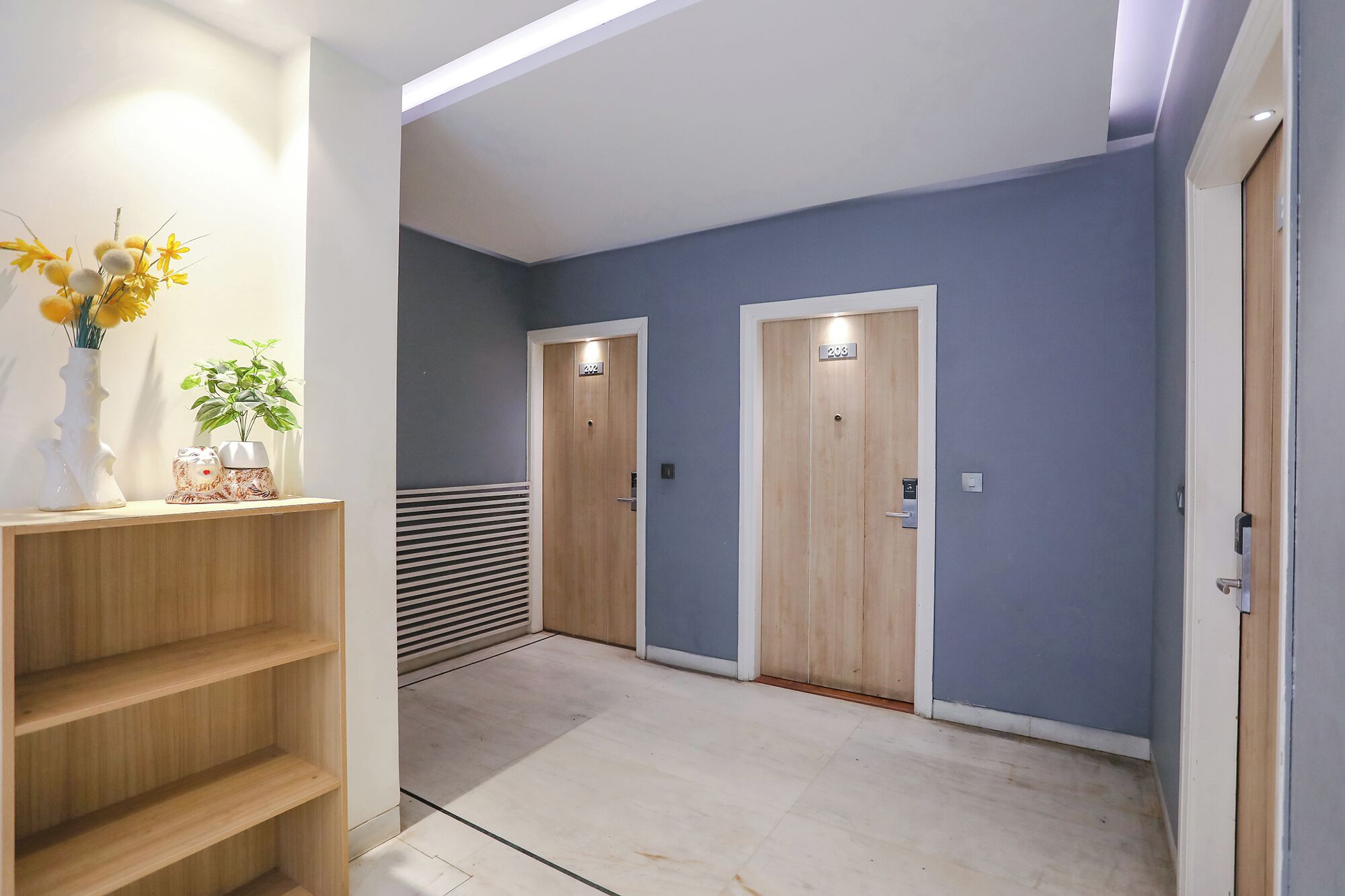 A hallway with two wooden doors, a white shelf with decorative items, and a vent on the wall.