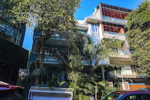 Un edificio a più piani con balconi, immerso tra alberi e automobili parcheggiate.