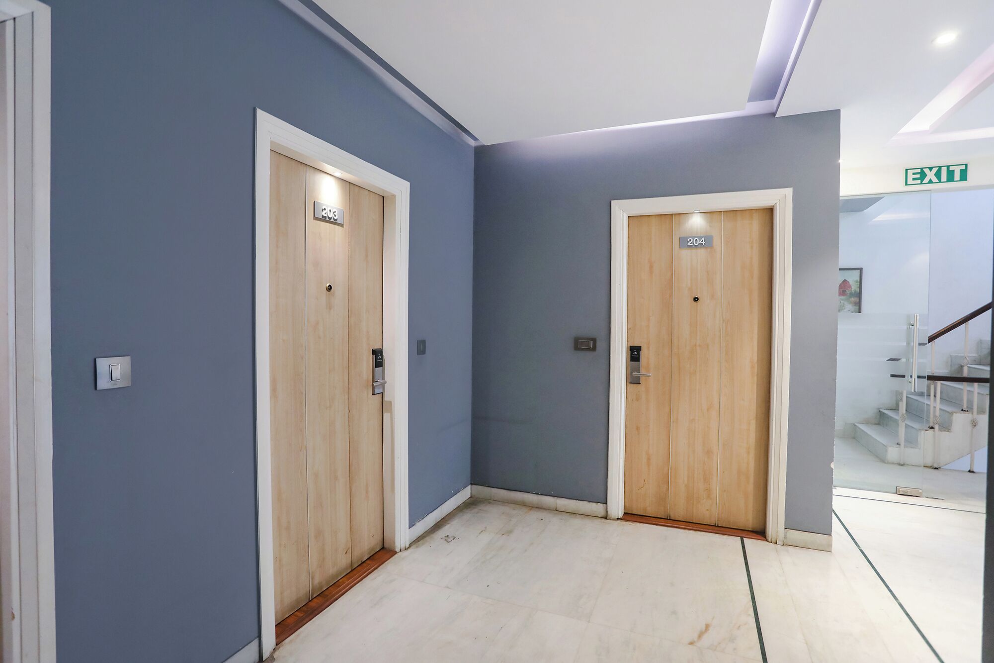 Two wooden doors with numbers 203 and 204, a light switch, and an exit sign.