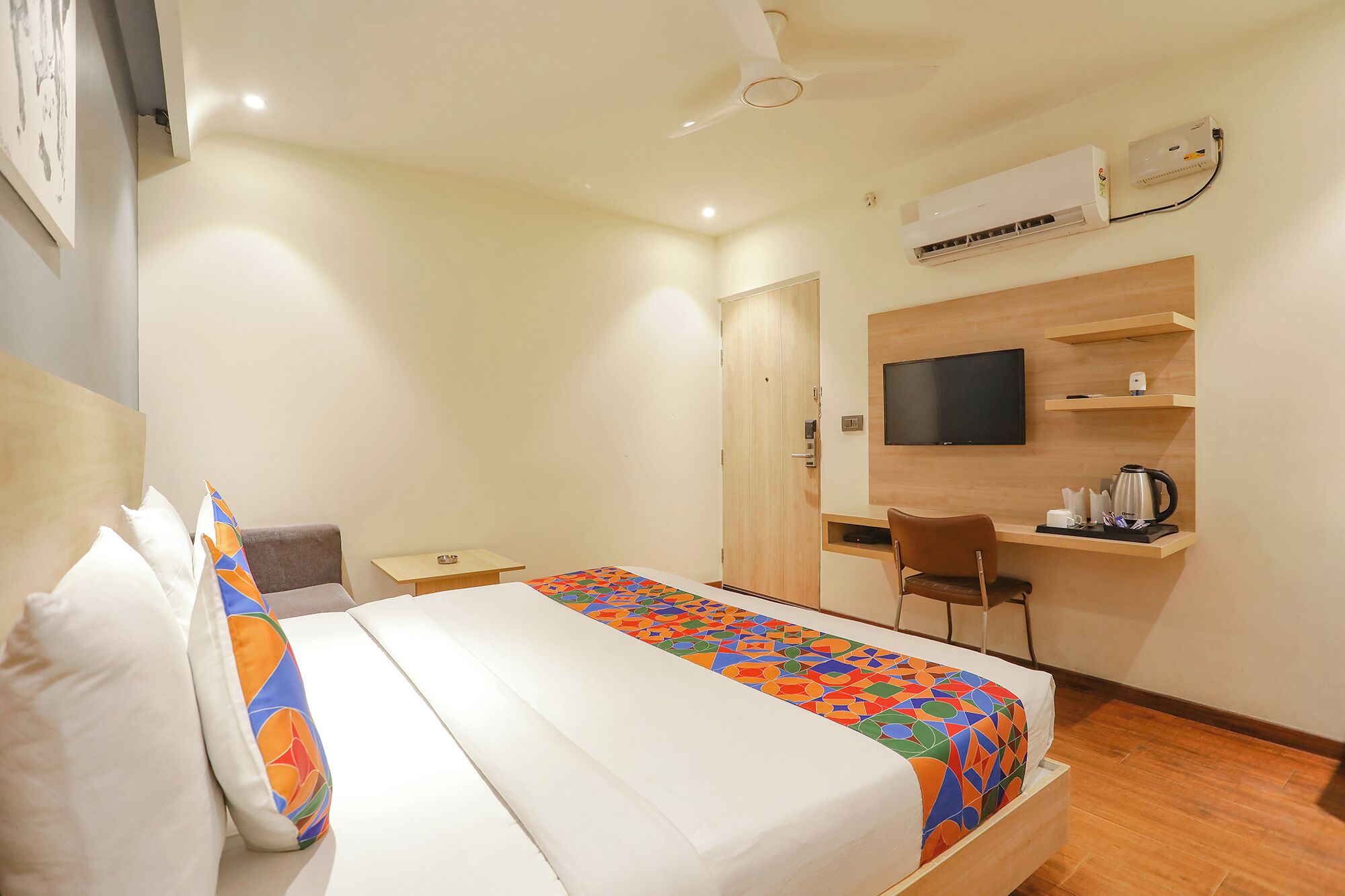 A hotel room with a bed, a desk, a chair, a television, and an air conditioning unit.