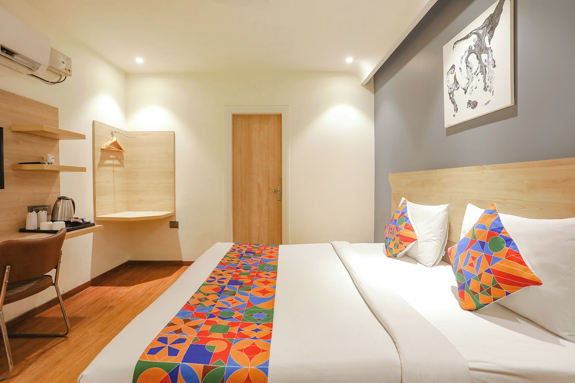 Ein Hotelzimmer mit einem Bett, einem Schreibtisch, einem Sessel, einer Holztür und einer Wand-Klimaanlage.