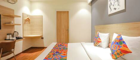 A hotel room with a bed, a desk, a chair, a wooden door, and a wall-mounted air conditioning unit.