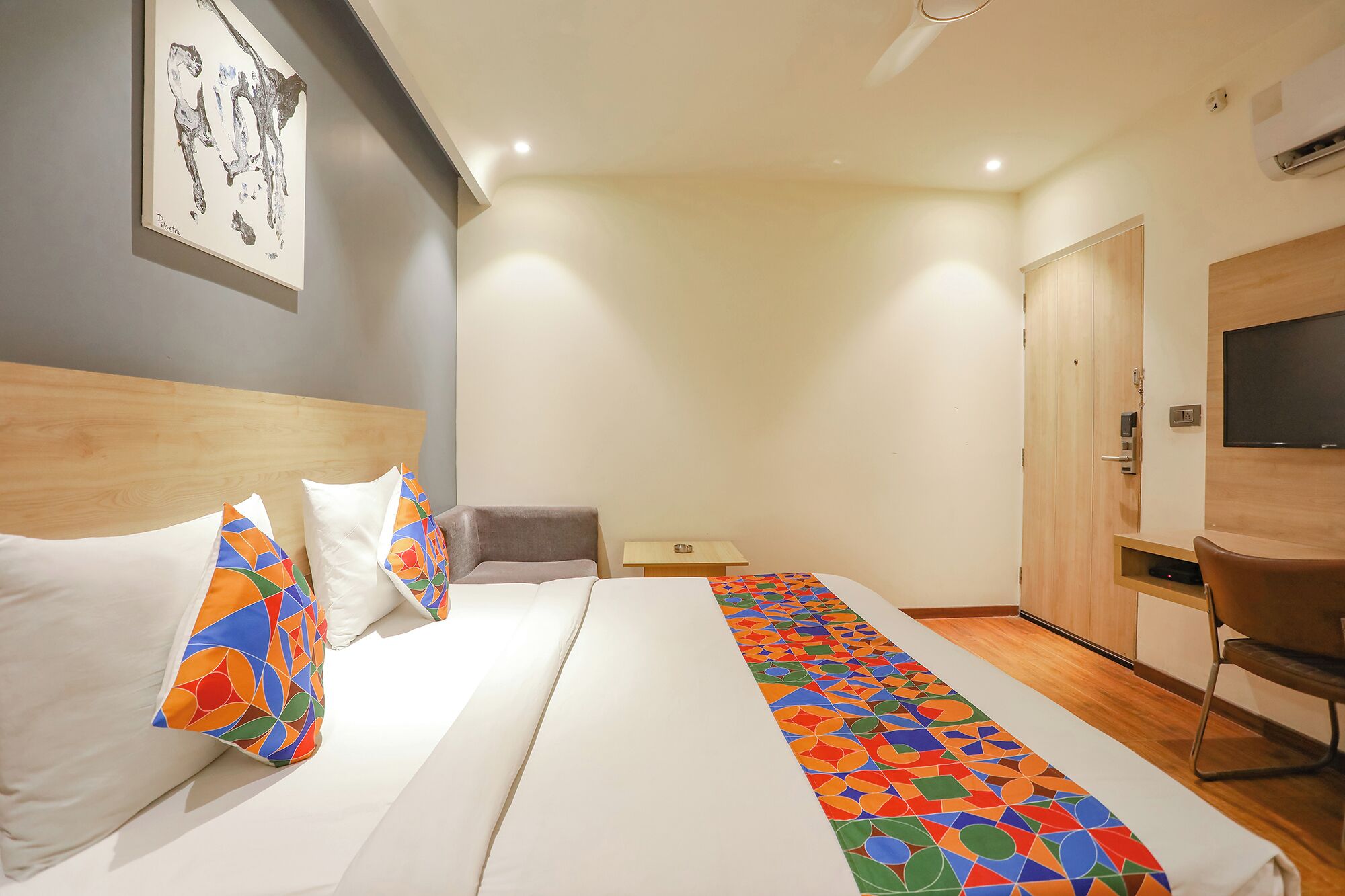 A hotel room with a bed, a desk, a chair, a TV, and a wardrobe.