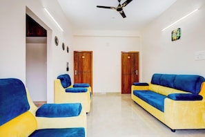 Una habitación con ventilador de techo, dos puertas de madera, un sofá y dos sillones.