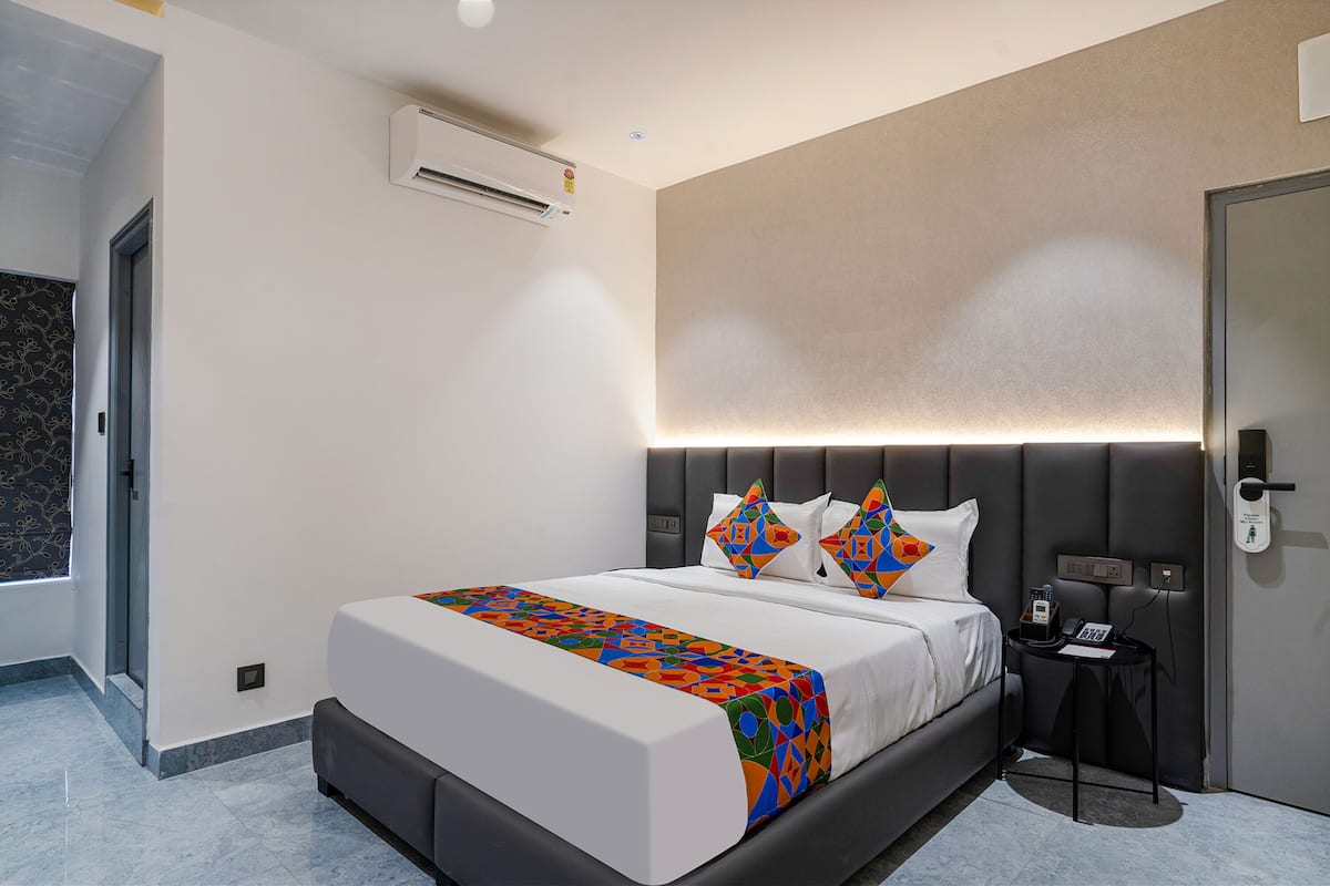 A modern hotel room with a large bed, a bedside table with a phone, and a wall-mounted air conditioner.
