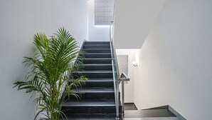 Una escalera moderna con barandilla de vidrio, una planta en maceta y una lámpara en la pared.