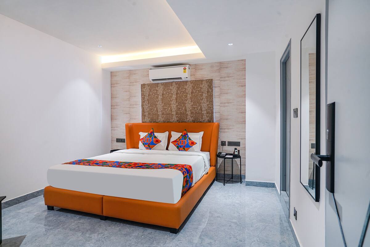 A modern hotel room with a large bed, an air conditioning unit, a bedside table, and a flat-screen TV mounted on the wall.