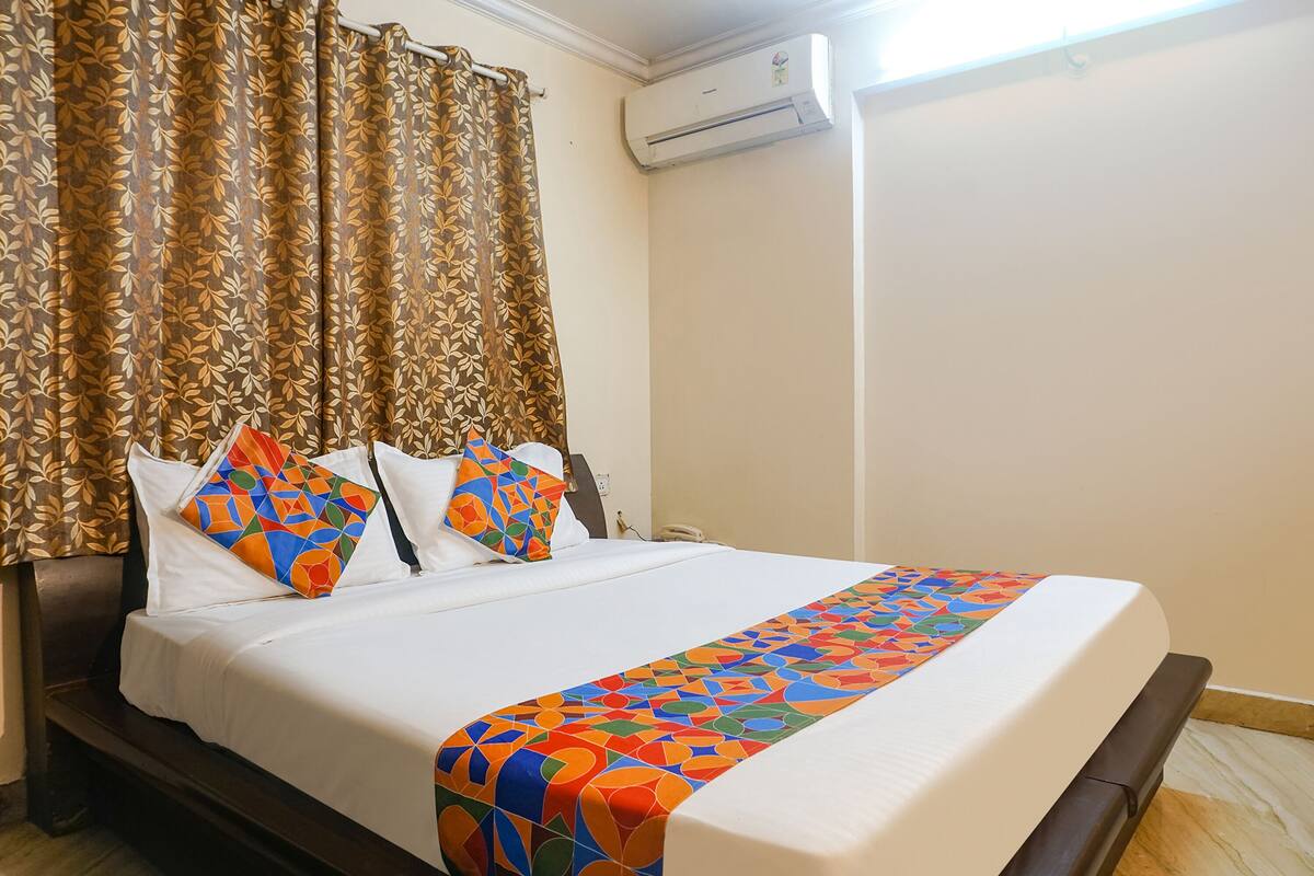 A hotel room with a bed, curtains, an air conditioning unit, and a patterned bedspread.