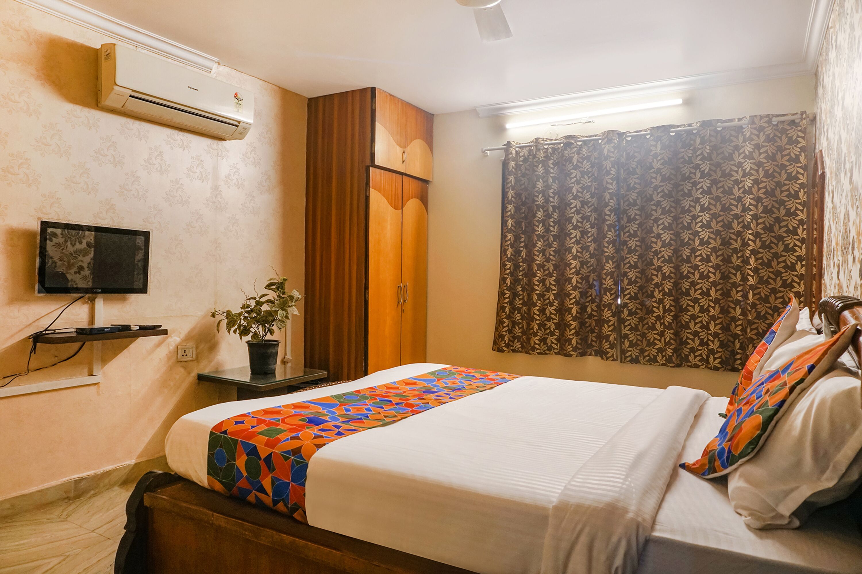 A hotel room with a bed, a wardrobe, an air conditioner, a TV, and a window with curtains.