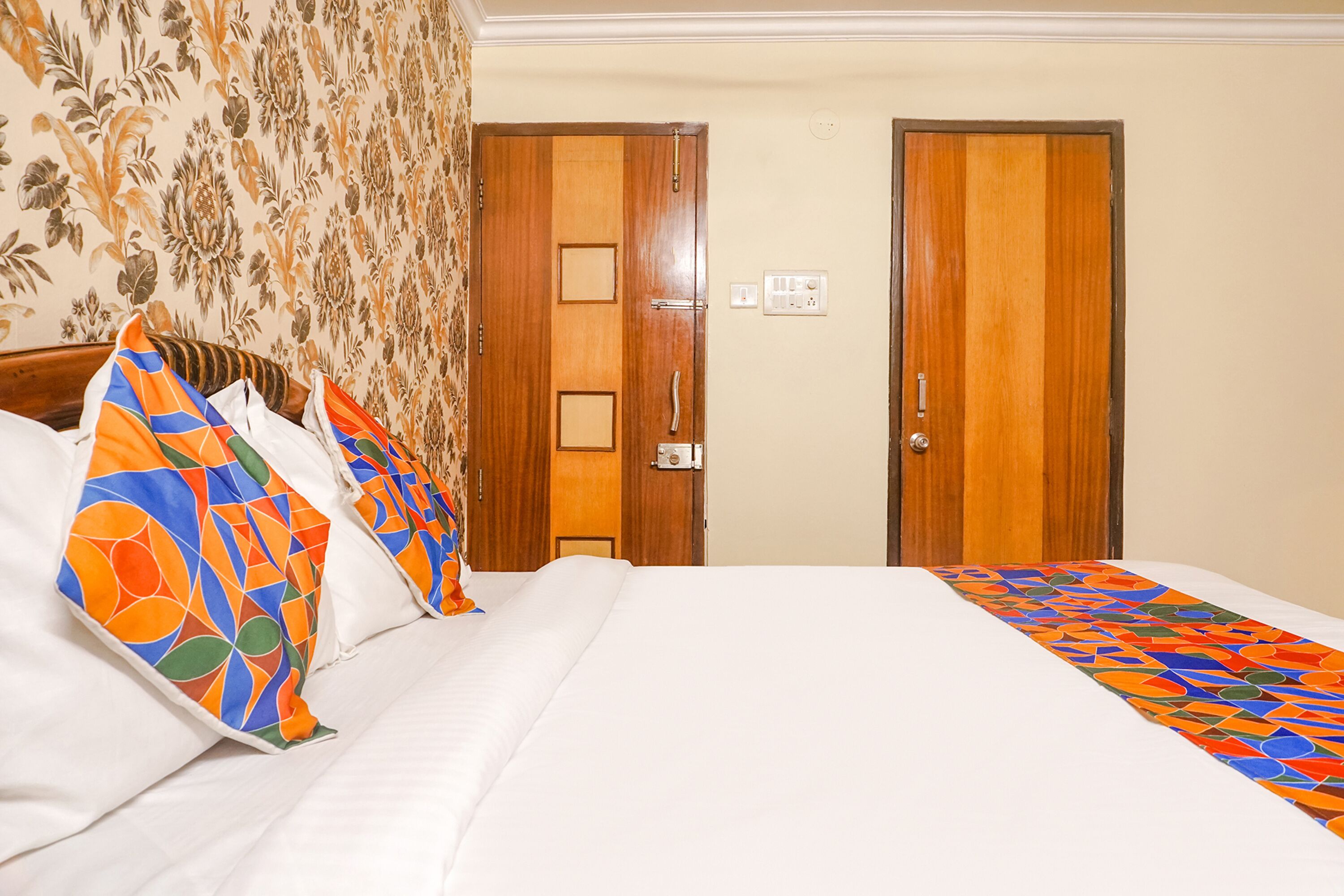 A hotel room with a bed, two doors, and a floral wallpaper pattern.