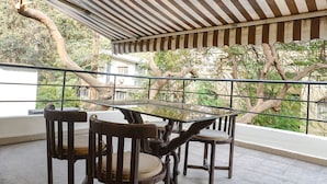 A balcony with a striped awning, a glass table, and wooden chairs. - Fabhotel Galaxy Residency (Pune)