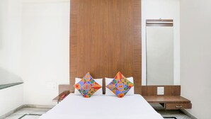 Une chambre d’hôtel avec un grand lit, deux coussins décoratifs, une tête de lit en bois, une table de chevet et un miroir.