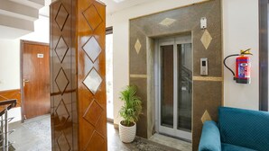 A lobby with a wooden door marked '101', an elevator, a fire extinguisher, and a blue sofa. - FabHotel The Indian (Gurugram)