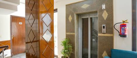 A lobby with a wooden door marked '101', an elevator, a fire extinguisher, and a blue sofa.