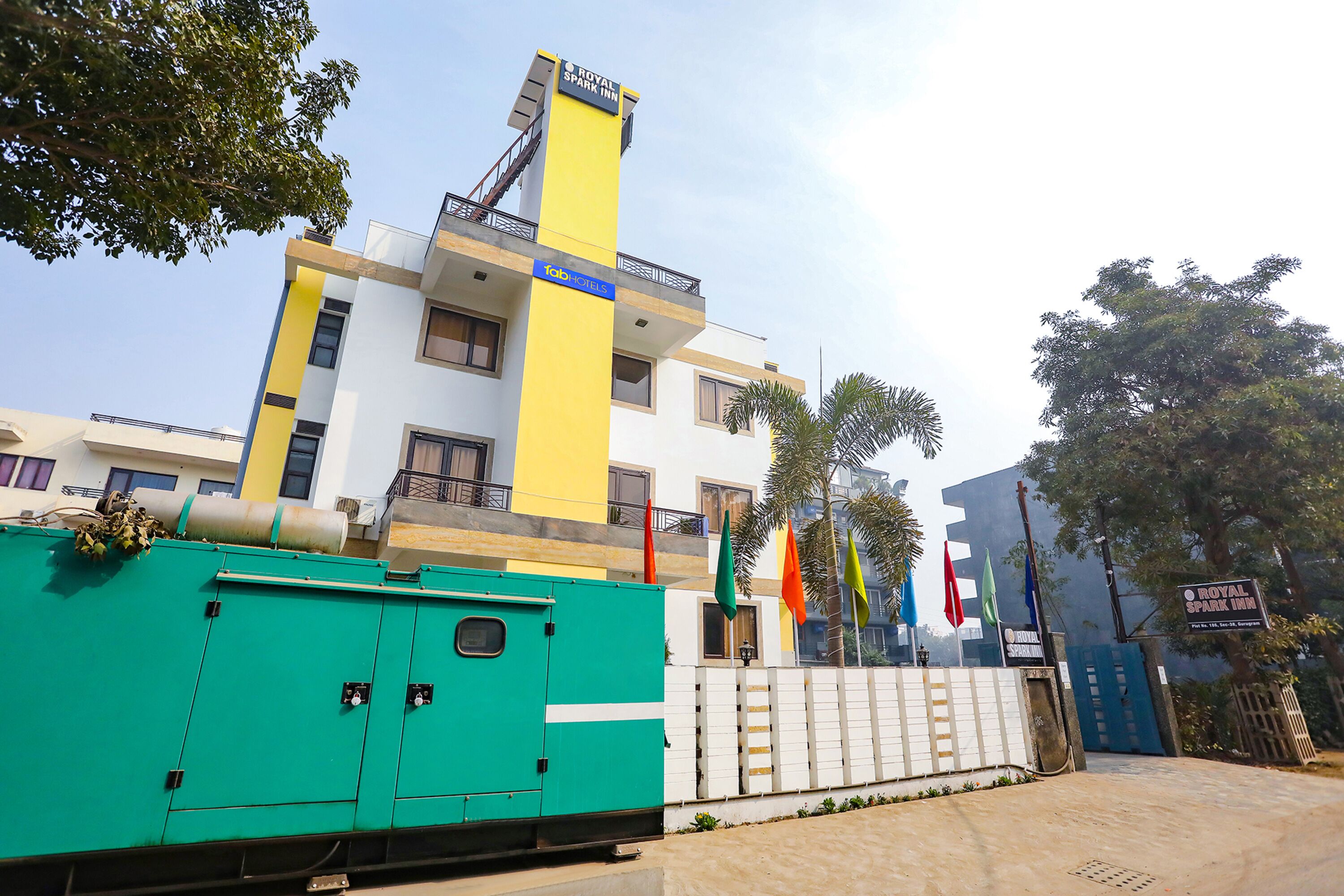 A hotel with a modern design, featuring a prominent yellow and white facade, multiple windows, and a visible entrance gate.