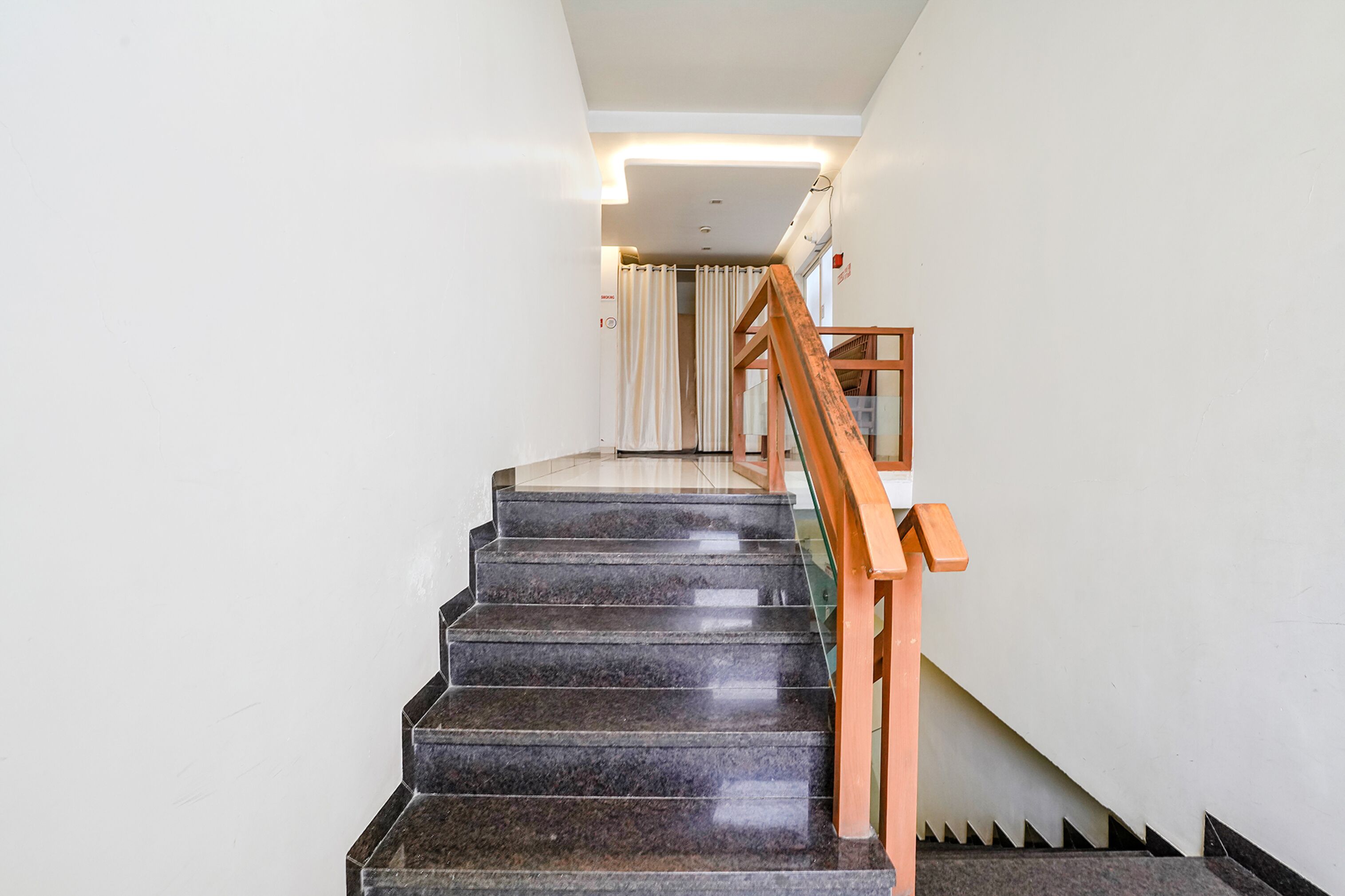 A staircase with dark marble steps and wooden handrails, leading to a room with a white ceiling and a light fixture.