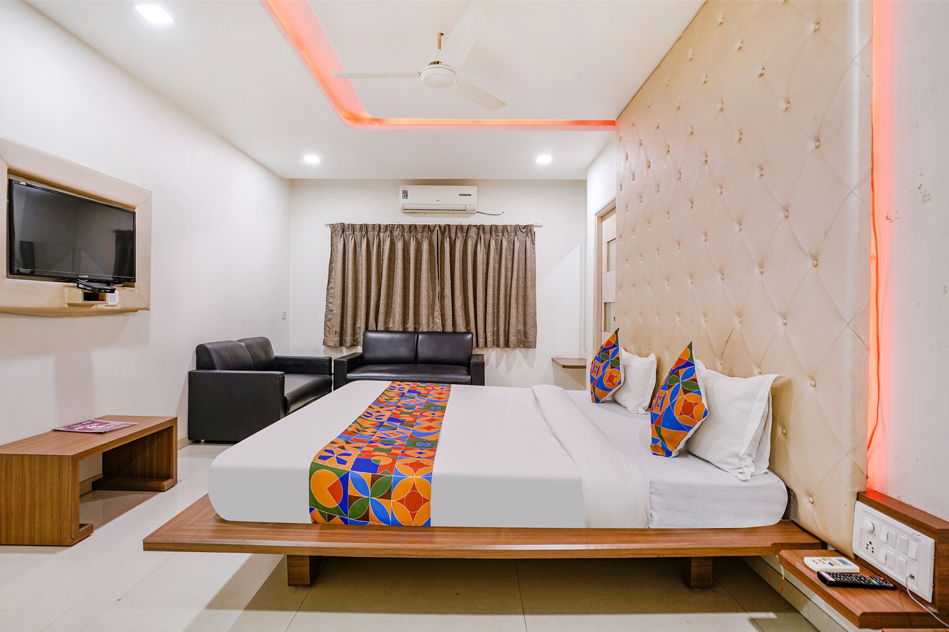 A hotel room with a bed, a desk, a chair, a TV, and an air conditioning unit.