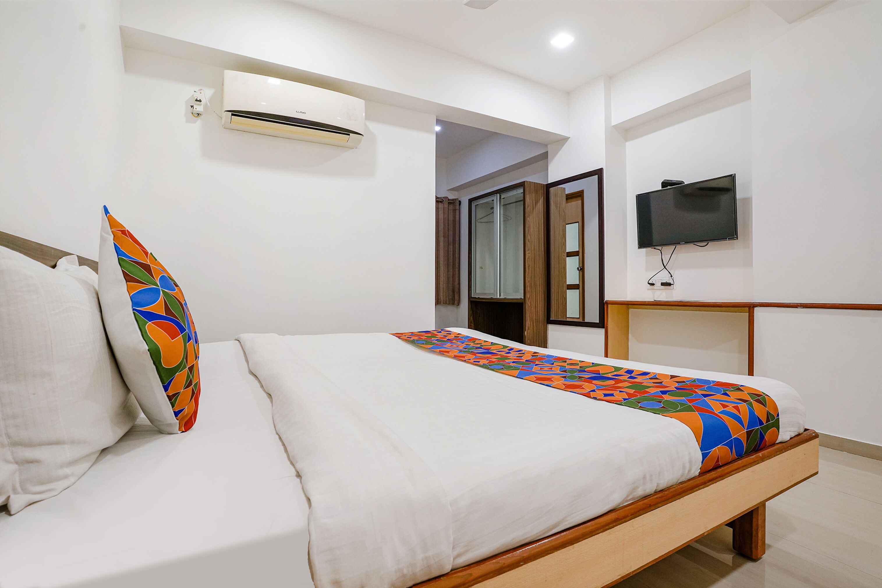 A neatly made bed with a colorful bedspread, a white pillow, and a matching pillow with a geometric pattern.