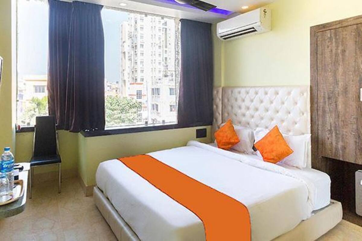 A hotel room with a bed, an air conditioning unit, a wardrobe, and a window with curtains.