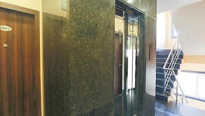 L’intérieur d’un bâtiment moderne présente une porte en bois portant l’inscription « 2003 », un mur en marbre et un escalier menant à un étage supérieur.