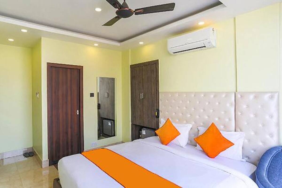 A hotel room with a bed, an air conditioner, a ceiling fan, and a wardrobe.