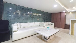 A modern living room with a white sofa, a glass partition with floral patterns, and a wooden coffee table. - Fabhotel Prime Zewarat Inn (New Delhi)