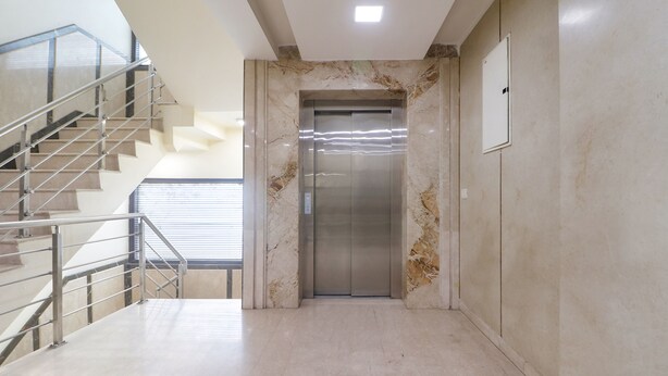 A modern elevator in a hallway with marble walls and a metal staircase. - Fabhotel Prime Zewarat Inn (New Delhi)