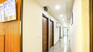 A hallway with wooden doors, a security camera, and a potted plant. - FabHotel Nirvana Residency (New Delhi)