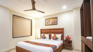 A hotel room with a large bed, a ceiling fan, a painting on the wall, and a small table with a plant. - FabHotel Nirvana Residency (New Delhi)