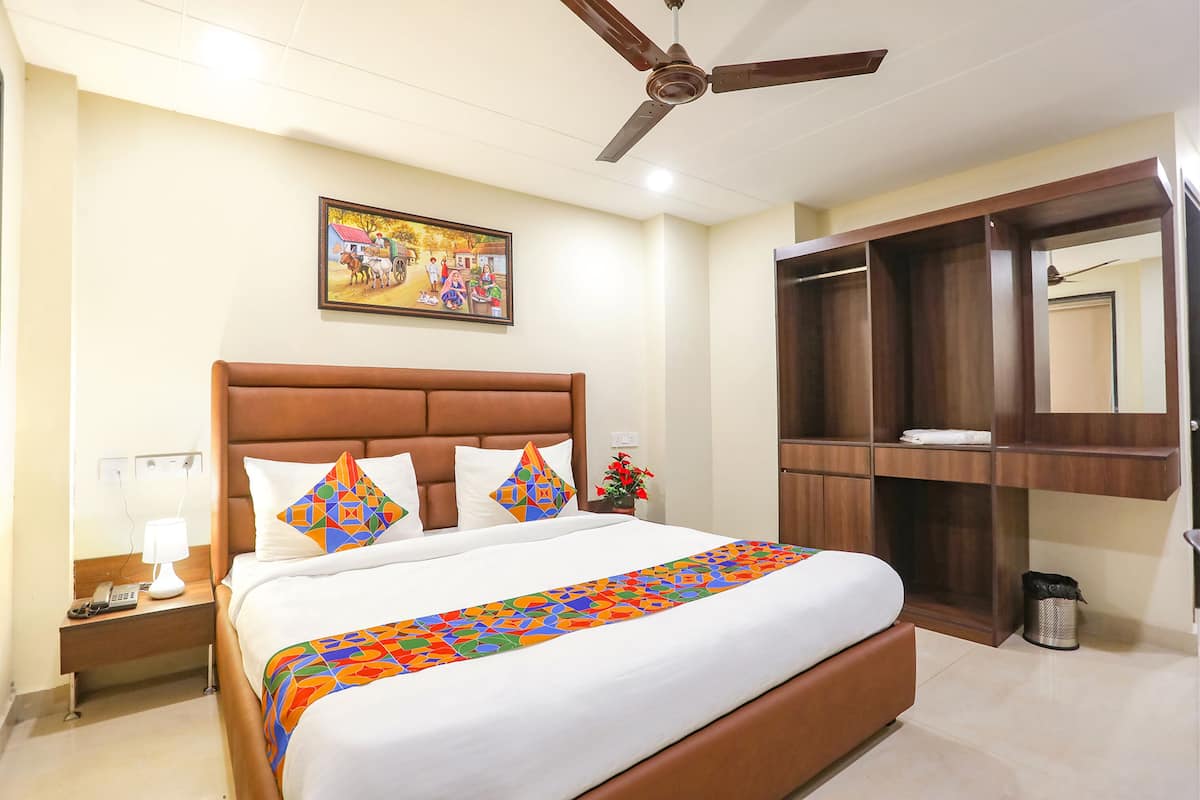 Una habitación de hotel con una cama grande, un ventilador de techo, una mesita de noche con lámpara, un cuadro en la pared y un armario.