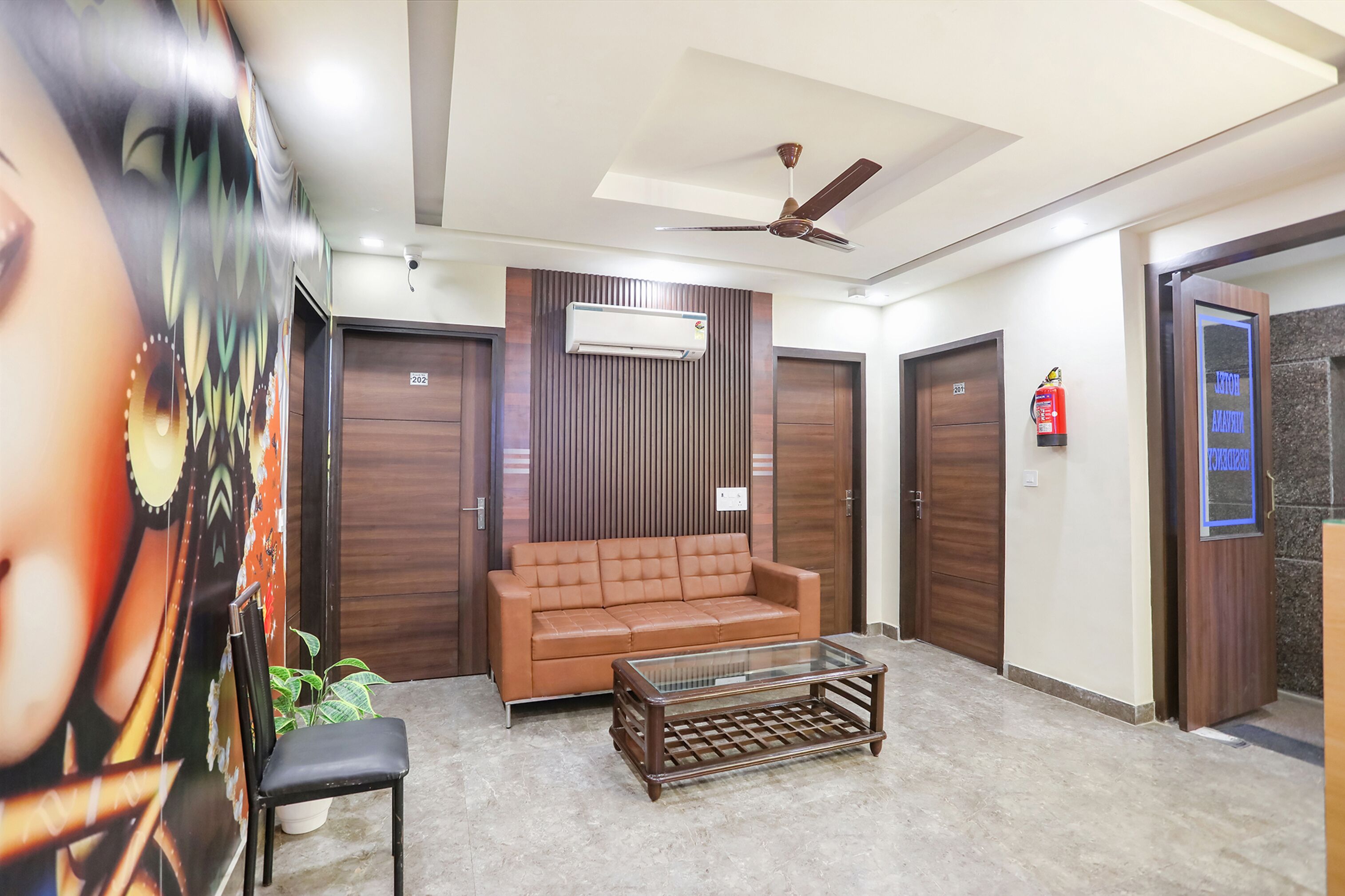 A lobby with a brown leather sofa, a glass coffee table, a ceiling fan, and wooden doors.