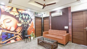 A modern living room with a sofa, a coffee table, a ceiling fan, and a wall mural. - FabHotel Nirvana Residency (New Delhi)