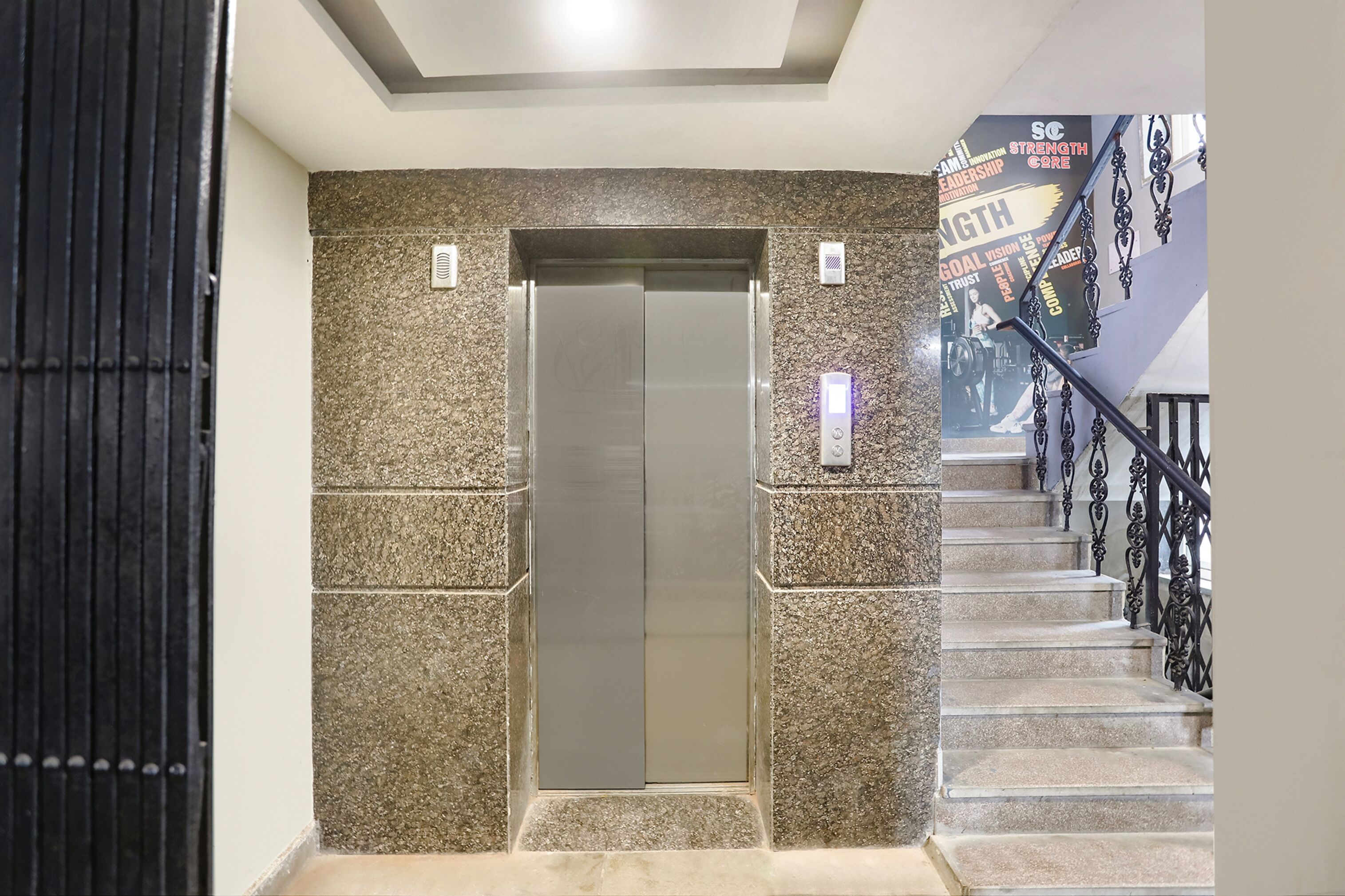 An elevator with a granite wall, a staircase with black railings, and motivational posters on the wall.