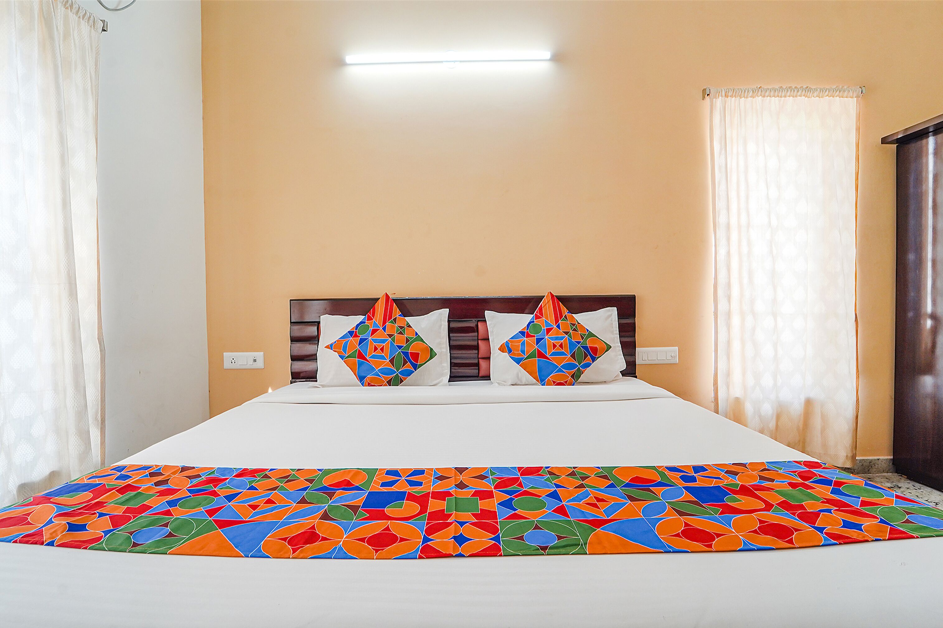 Una cama con un edredón de estampado geométrico y colores vivos, un cabecero de madera y dos almohadones decorativos.