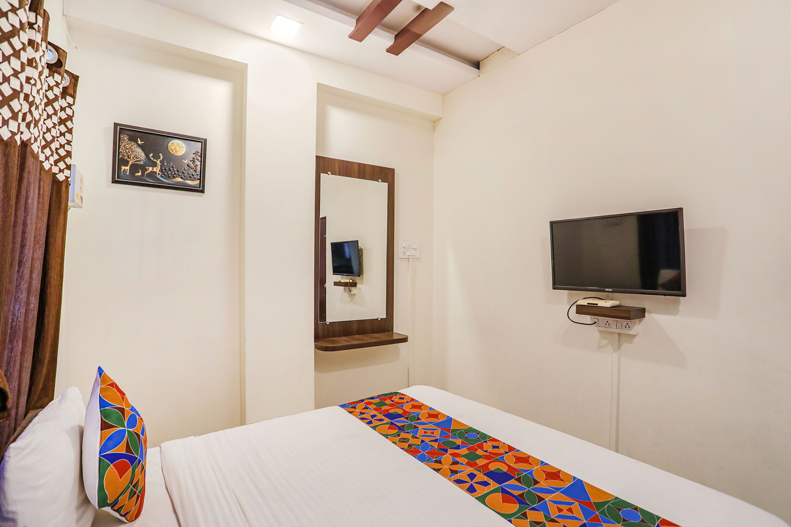 Habitació d'hotel amb un llit, una televisió penjada a la paret, un mirall i un coixí decoratiu.