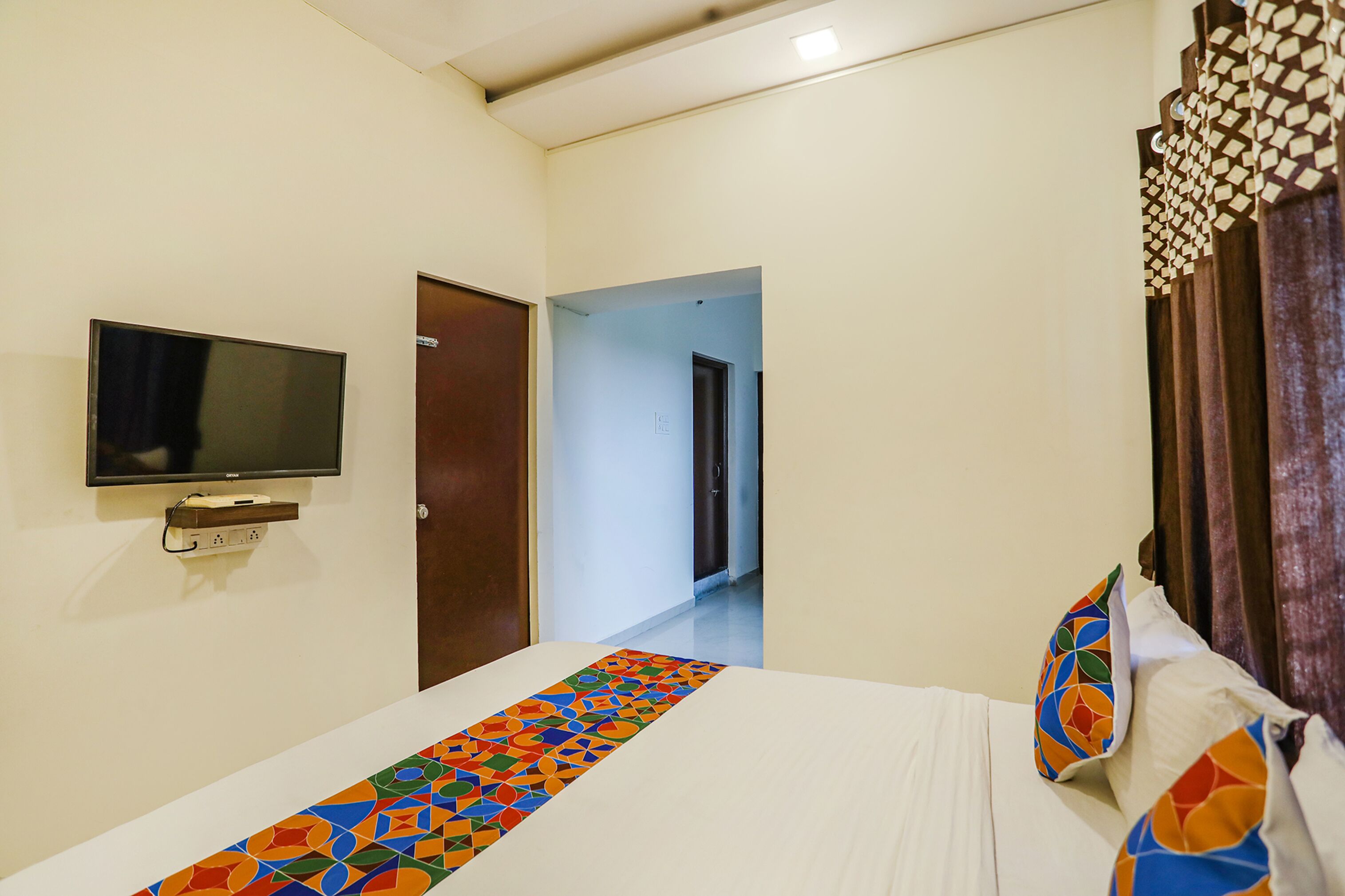 A hotel room with a bed, a television mounted on the wall, and a door leading to another room.