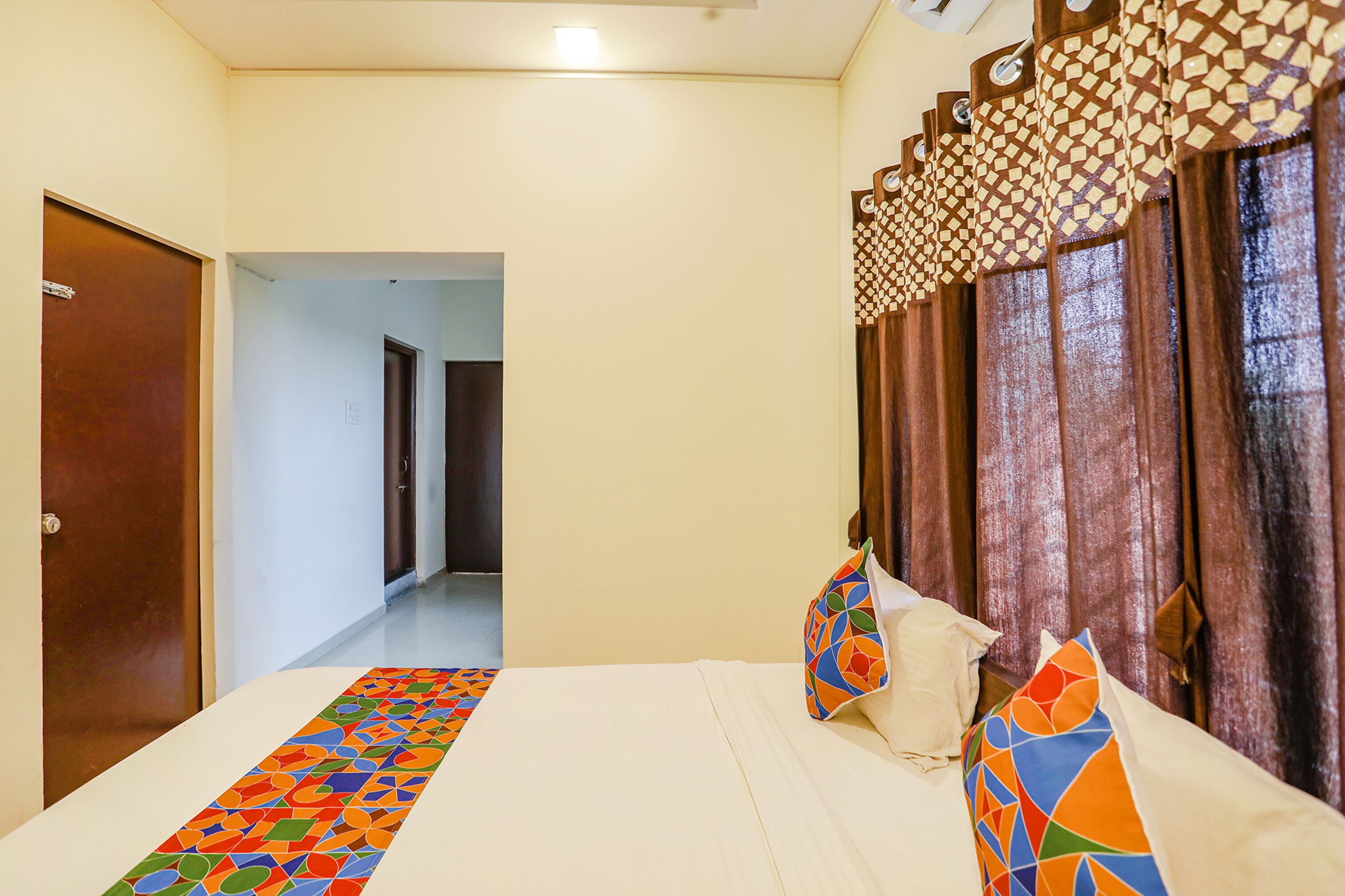 A hotel room with a bed, a patterned bed runner, a door, and a view of a hallway.