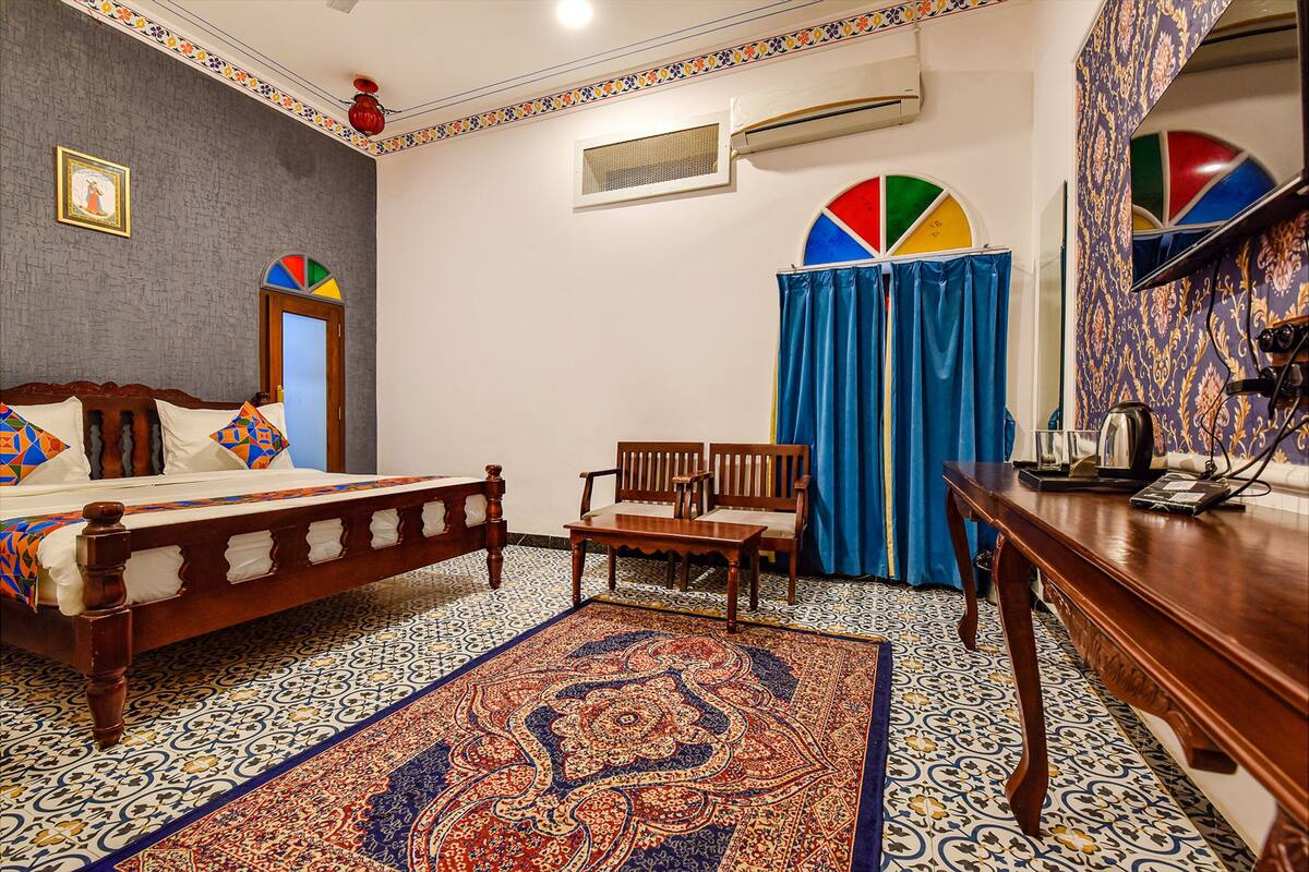 Une chambre à coucher avec un lit, une chaise en bois, une table, un tapis coloré et un sol à motifs.
