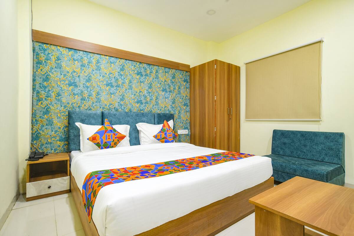 A neatly arranged bedroom with a bed, a nightstand, a wooden wardrobe, a blue sofa, and a wooden table.