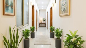 A hallway with potted plants, framed artwork, and a lamp table. - FabHotel Grand Giriraj (Indore)