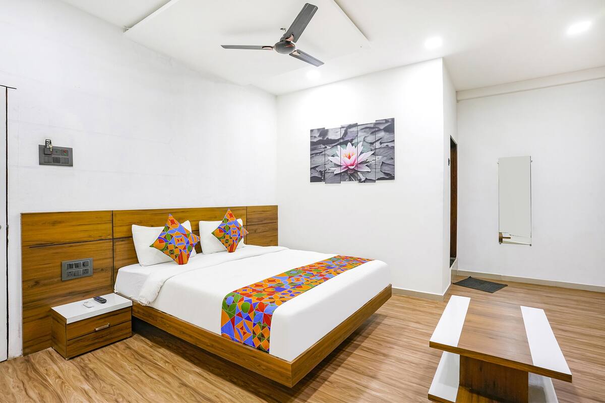 A hotel room with a wooden bed, a ceiling fan, a wall-mounted TV, and a wooden nightstand.