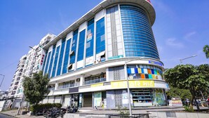A multi-story commercial building with a curved corner design, featuring large windows and a prominent sign at the ground level. - Fabhotel 7 Star (Surat)