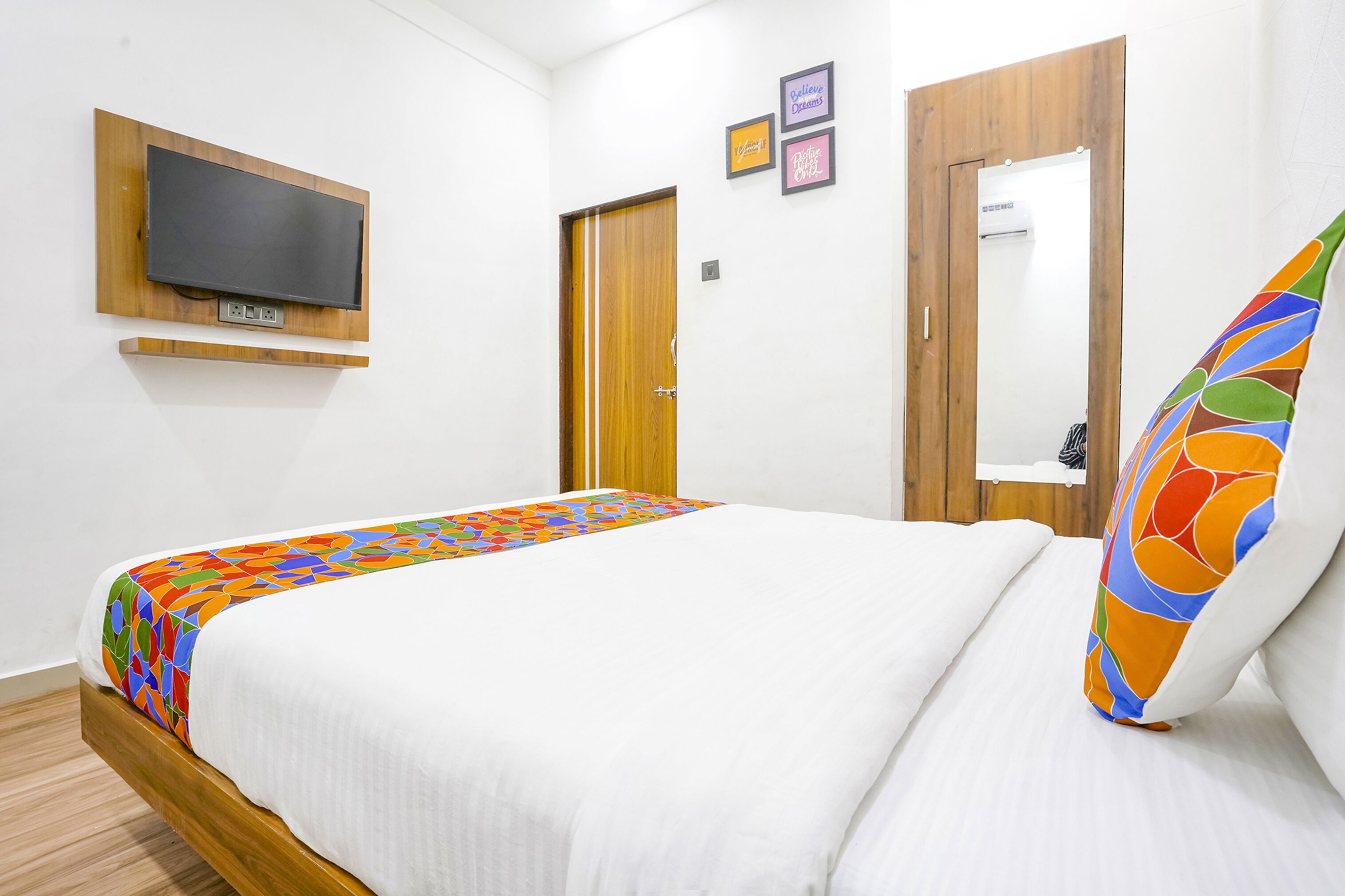 Habitación de hotel con una cama, televisor montado en la pared, puerta de madera y un espejo.